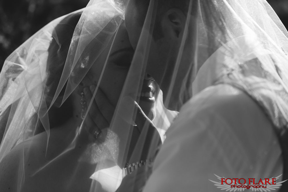 B&W photo of the bride and groom kissing under veil