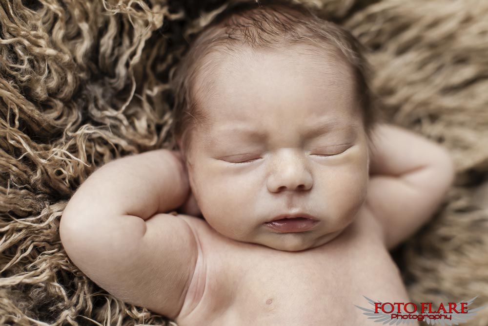 Sleeping newborn with arms behind their head
